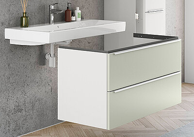 Moderne Badezimmer-Waschtisch mit klaren Linien, einem weißen Waschbecken, Salbeigrün und weißen Schubladen, vor einer strukturierten grauen Wand.