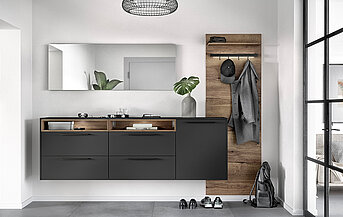 Modernes Badezimmerinterieur mit schlankem anthrazitfarbenem Waschtisch, Holzakzenten und minimalistischer Dekoration, das einen eleganten und zeitgenössischen Wohnraum vermittelt.