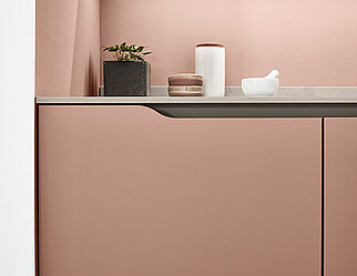 Zeitgemäßes Küchendesign mit einer eleganten Arbeitsplatte und minimalistischer Dekoration vor einem sanft rosa Hintergrund, das Funktionalität mit einem modernen ästhetischen verbindet.