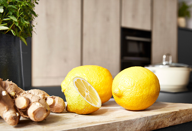 Frische Zitronen und Ingwerwurzel auf einem hölzernen Schneidebrett, was auf gesunde Zutaten in einer modernen Kücheneinstellung hinweist.