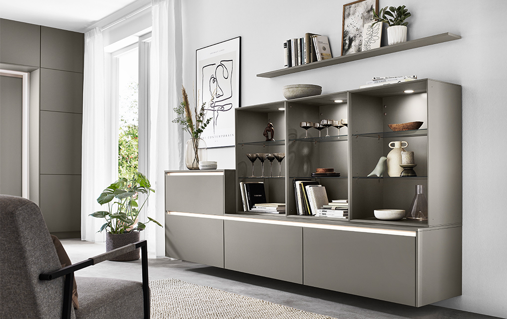 Modernes Wohnzimmerinterieur mit schlanken modularen Regaleinheiten, die Bücher und Dekorationen anzeigen, ergänzt durch minimalistische Möbel und natürliches Licht.
