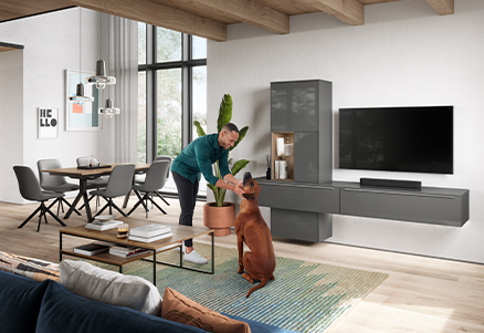 Ein Mann spielt in einem modernen Wohnzimmer mit einem lebhaften braunen Hund, umgeben von eleganten Möbeln, Holzakzenten und einem einladenden, zeitgemäßen Designästhetik.